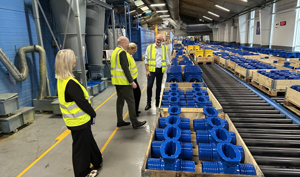En gruppe personer i gule veste ser på blå metalemner i en fabrikshal.